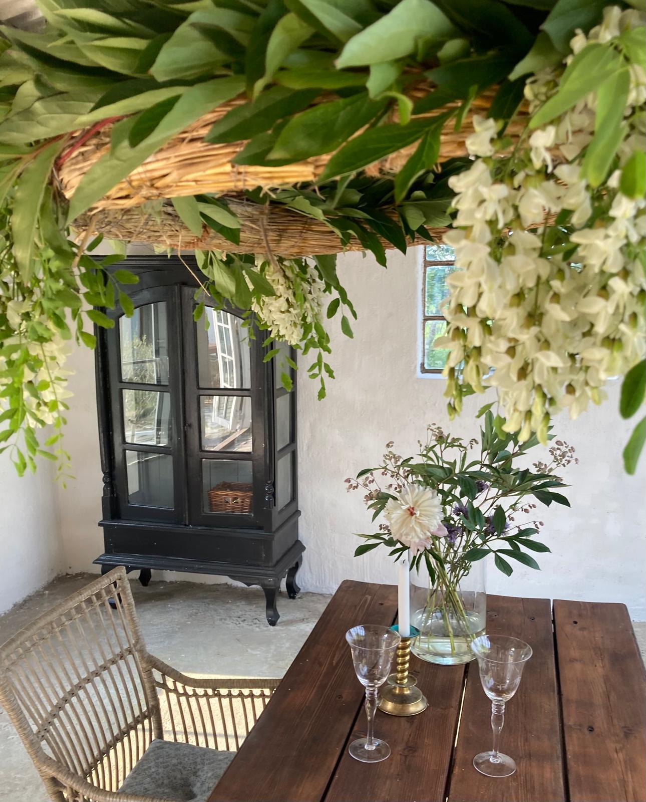 Uteplats med träbord, blommor och vinglas under hängande grönska